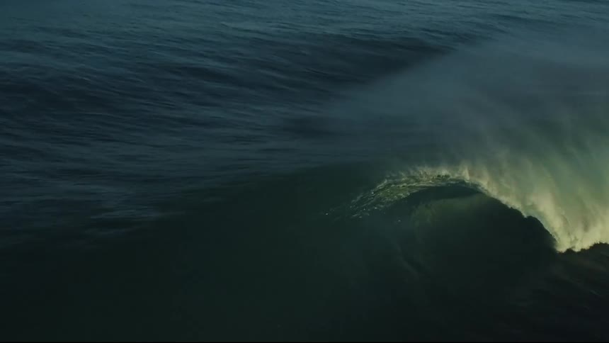 A powerful dark ocean wave crests and barrels in dramatic slow motion