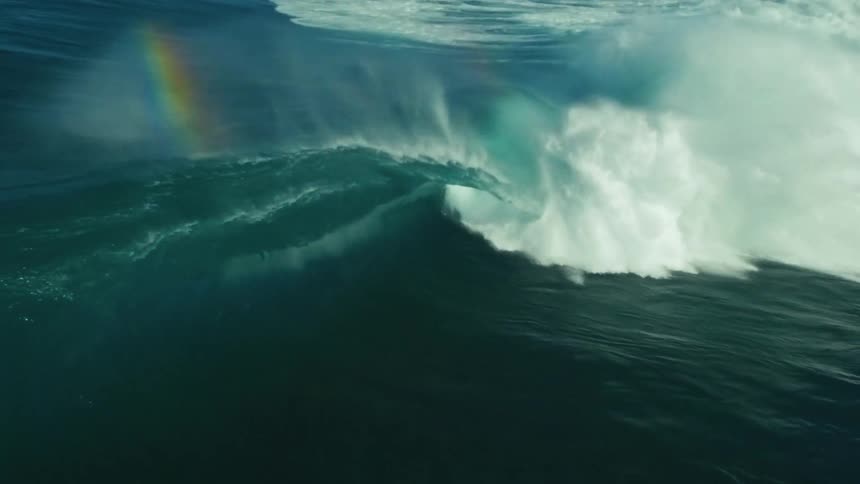 Super slow motion footage shows a majestic ocean wave curling and crashing with a rainbow visible in its spray