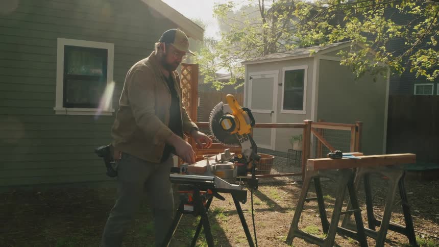 A skilled carpenter meticulously prepares to cut a piece of lumber with a miter saw in a sun-drenched backyard