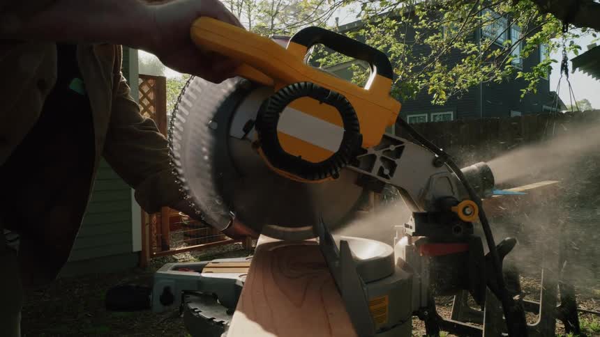 In a dramatic slow-motion close-up, a powerful miter saw blade slices through a wooden plank, sending a cloud of sawdust into the sunlit air