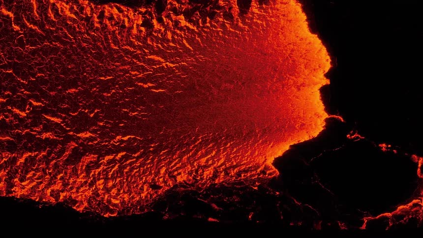 Intense aerial view of a fiery river of molten lava flowing in the darkness