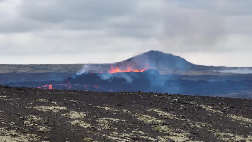 A slow tilt down reveals a dramatic volcanic eruption with spewing lava and smoke in a barren, rocky landscape