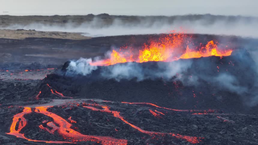 Dramatic slow-motion footage shows a volcanic fissure erupting with fiery lava fountains and rivers of molten rock across a dark landscape