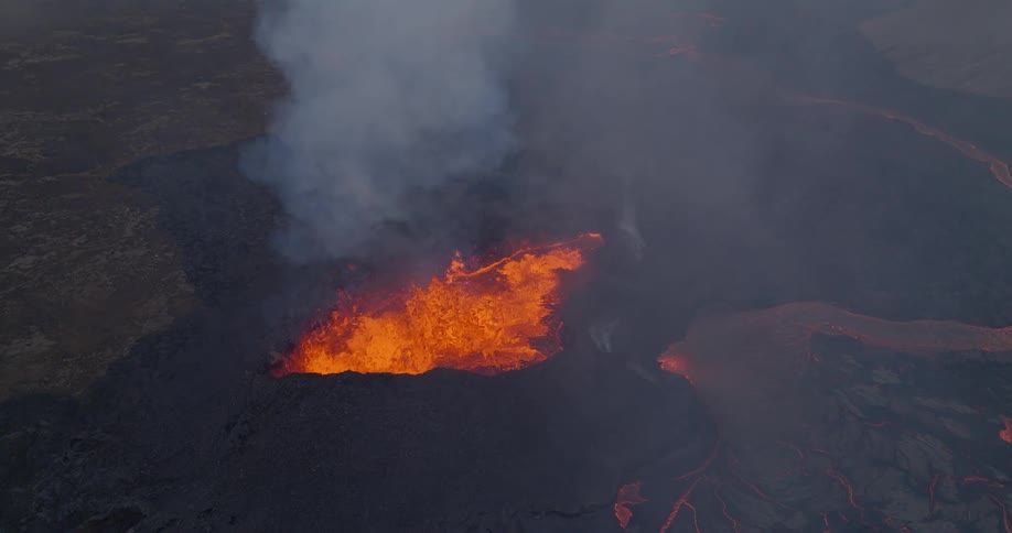 A powerful aerial shot tilts down over a smoking volcano, revealing the fiery, bubbling lava inside the crater