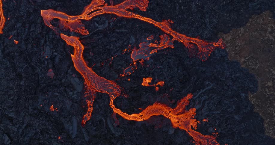 A mesmerizing top-down aerial view shows rivers of vibrant orange molten lava flowing across a dark, hardened volcanic landscape