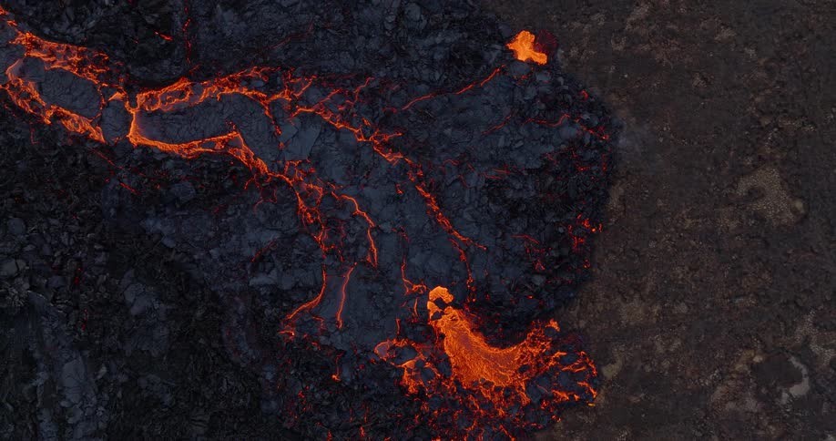 A mesmerizing top-down aerial view of a fiery river of molten lava flowing across a dark, solidified volcanic landscape