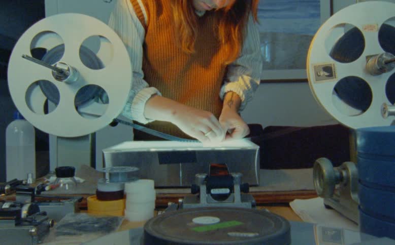 A filmmaker carefully inspects and splices a strip of movie film on a vintage light table in a dark editing room