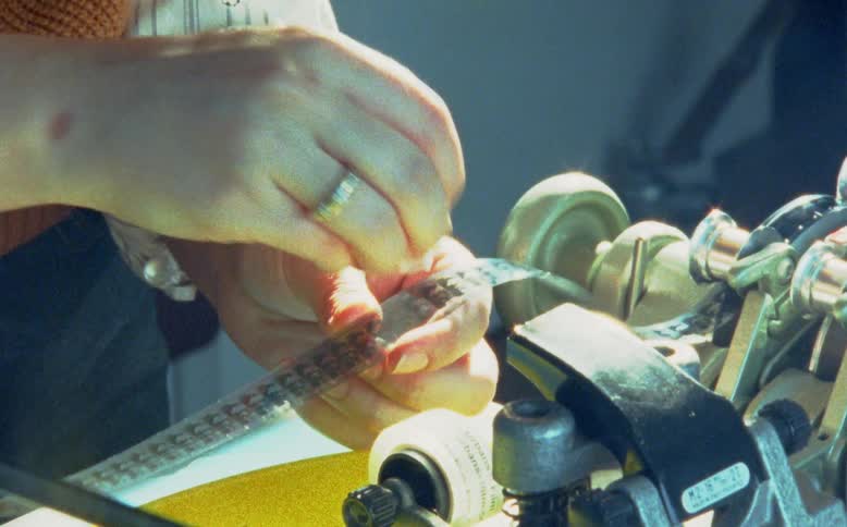 A film editor carefully inspects and cleans a strip of vintage motion picture film