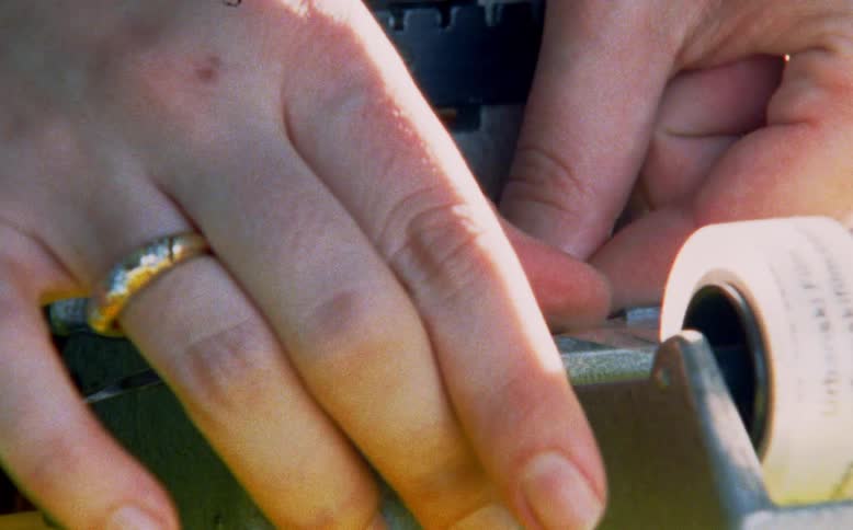 An editor's hands carefully cut and tape a strip of celluloid film on a vintage splicer