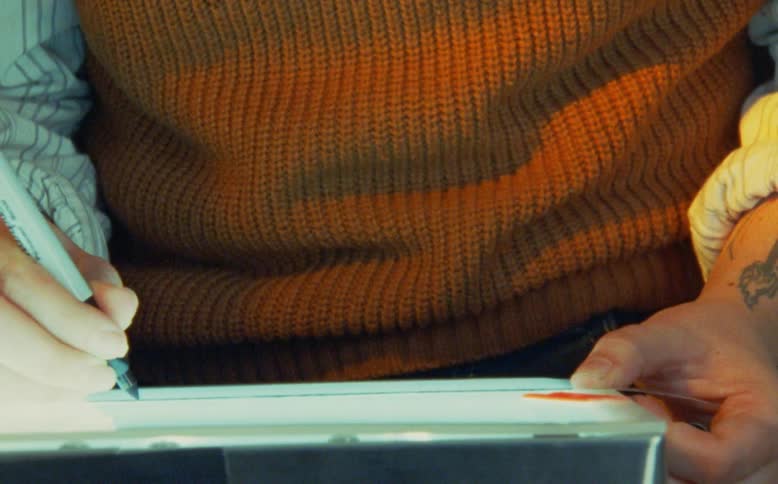 Close up of an artist with a tattoo wearing a warm sweater carefully tracing a line with a marker and ruler on a light box