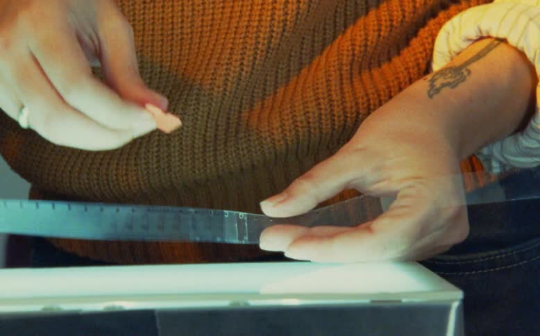 A filmmaker carefully splices together two pieces of analog filmstrip over a bright lightbox