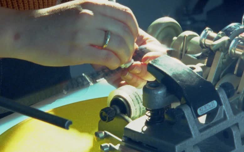 A film editor's hands meticulously clean a 16mm film strip running through a synchronizer machine