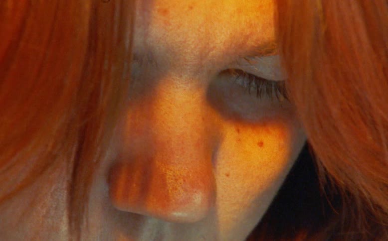 Extreme close-up on a pensive woman with vibrant red hair, her face illuminated by warm golden light in a vintage-style shot