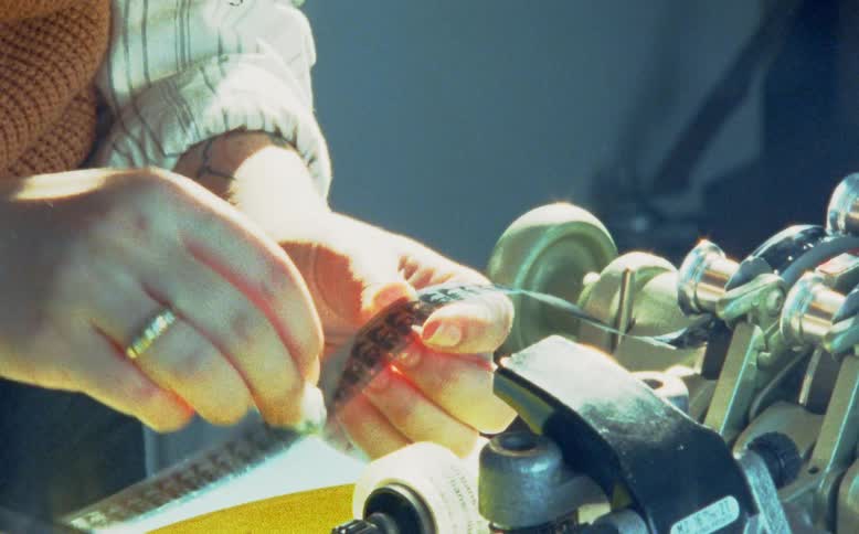 A close-up shot of a person's hands carefully cleaning a vintage 8mm film strip on an analog editing machine