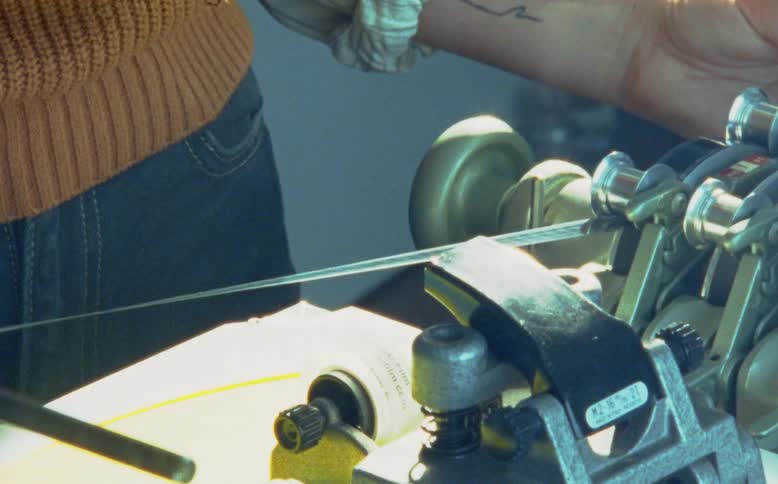 A close-up of a vintage film strip running through the sprockets of a synchronizer machine