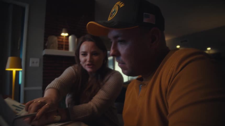 A veteran and his wife seriously discuss their finances at the dining table at night, analyzing charts on paper and a laptop