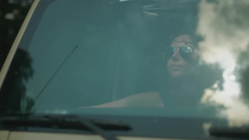 A woman is riding in a car wearing sunglasses