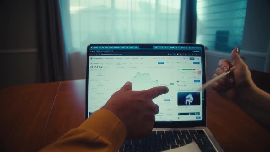 A man and woman analyze a cryptocurrency stock chart on a laptop, pointing at the screen and discussing their investment