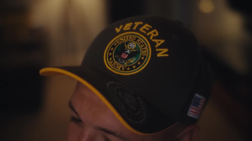 A close-up shot of a person wearing a black United States Army Veteran baseball cap with an American flag on the side