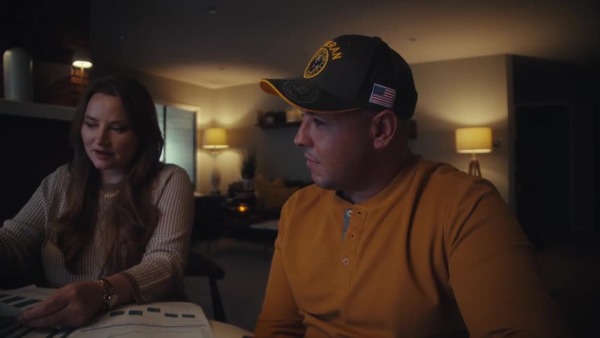 A military veteran and his wife sit together at a table in their home at night, reviewing important documents