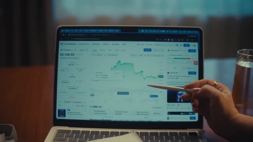 A man and woman collaborate while analyzing a fluctuating cryptocurrency financial chart on a laptop screen