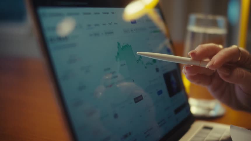 A close-up shot of a person using a stylus to analyze the Ethereum cryptocurrency price chart on a laptop
