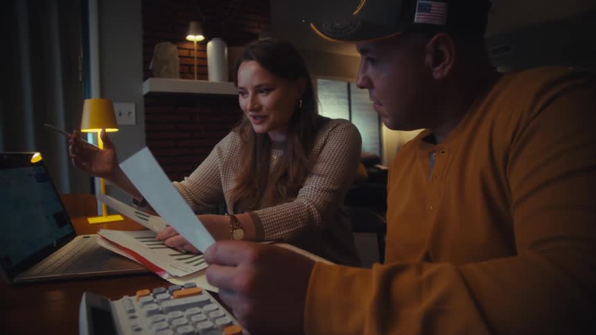 A couple works together on their household finances at night, using a laptop and charts to plan their budget