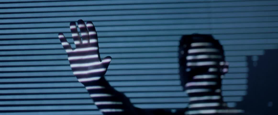 A man holds his hands up to shield his eyes from lines of light
