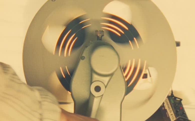Close-up shot of a hand operating a vintage film rewinder, with a warm light flickering through the spinning reel