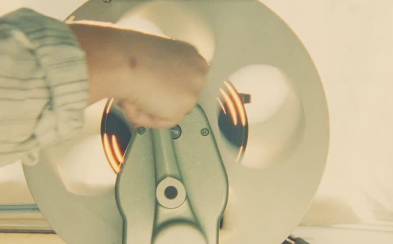 A close-up of a hand manually rewinding a film reel on a vintage editing machine