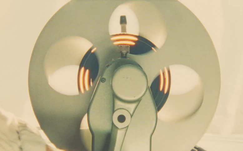 Close up of a hand manually operating a vintage film rewinder as the shiny reel spins rapidly