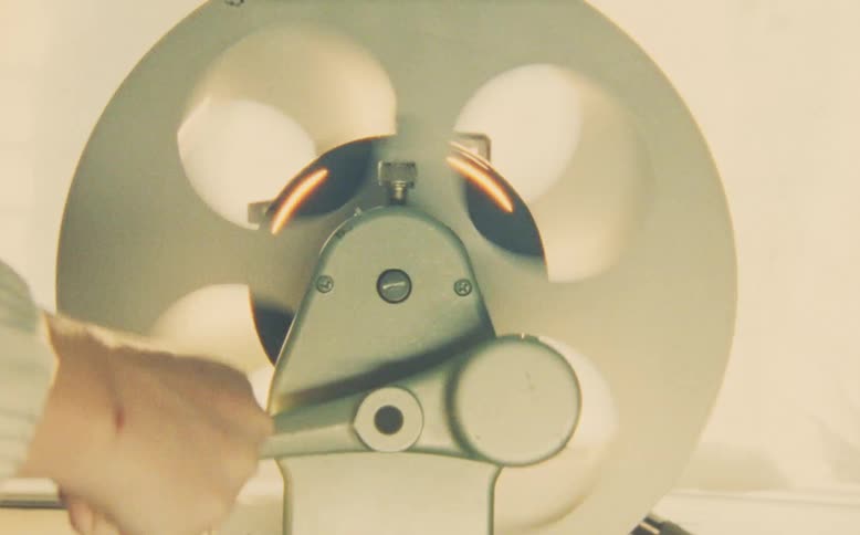 A close-up of a person's hand manually rewinding a vintage film reel on an editing machine