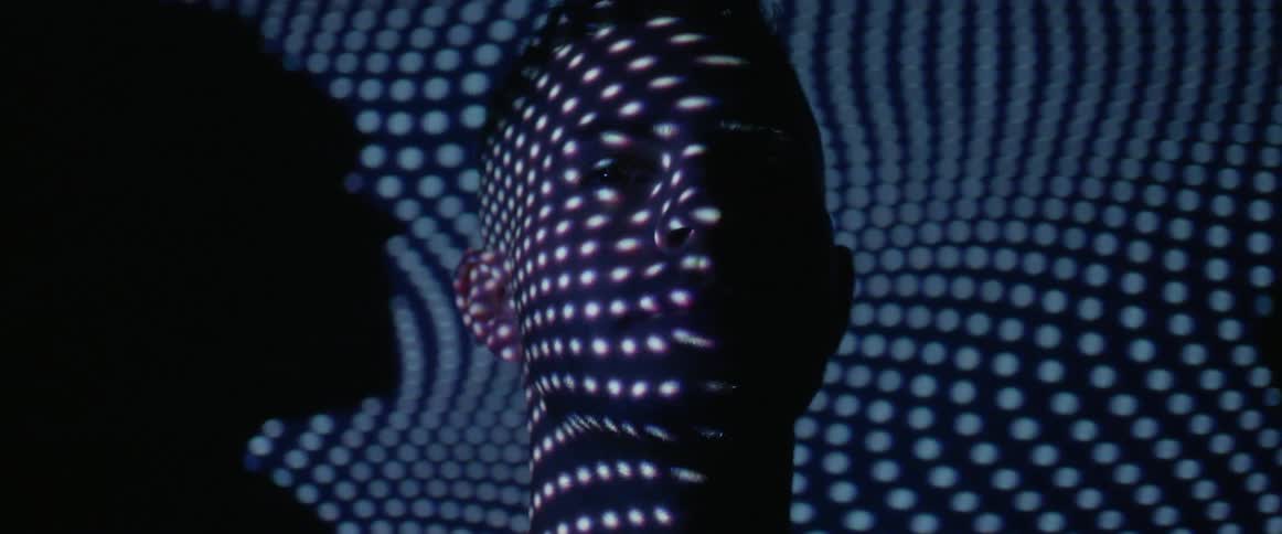 A man stands in a dark room with lights flashing on his face