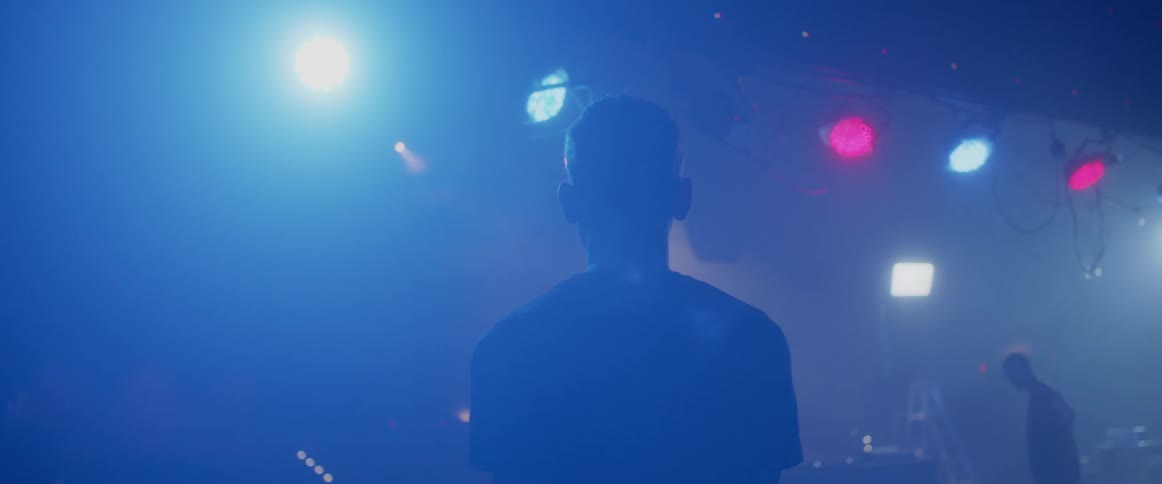 A man stands on a dark stage under lights