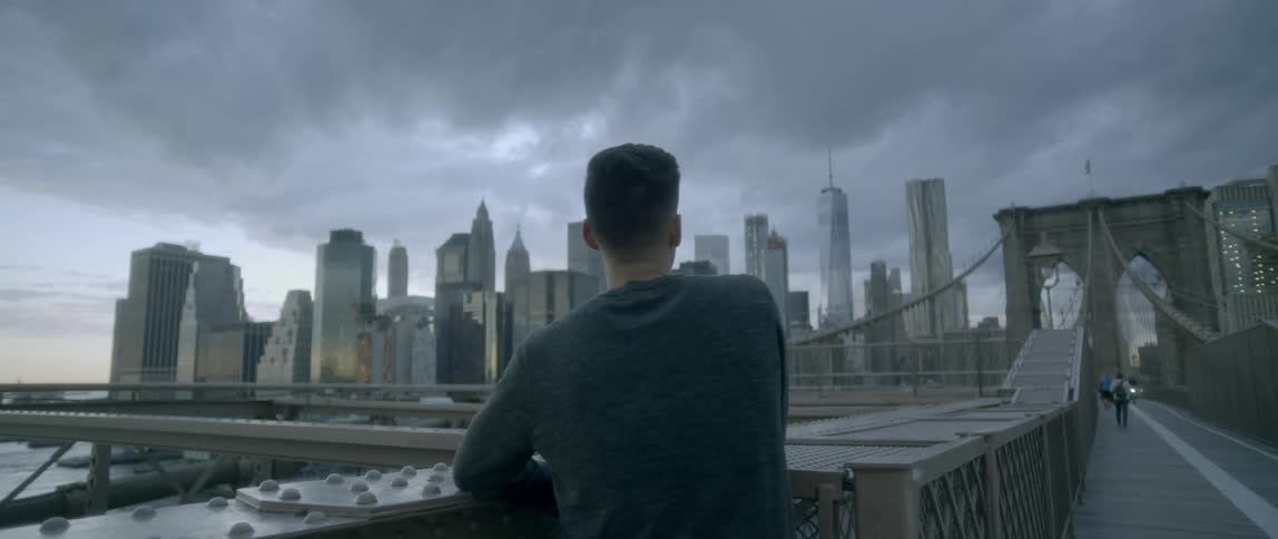A man stands on a bridge overlooking the city