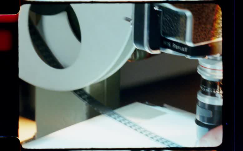 Close-up of a person inspecting a 16mm film strip with a loupe on a light table