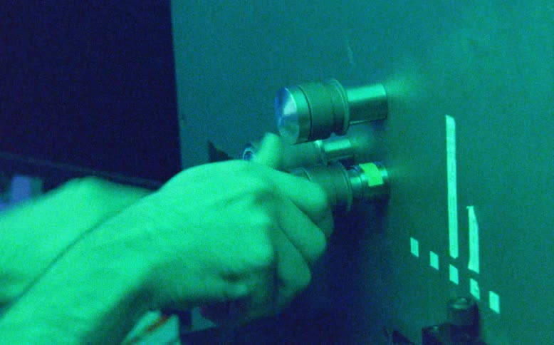 Vintage footage of a researcher adjusting optical equipment in a dark laboratory with shifting colored lights