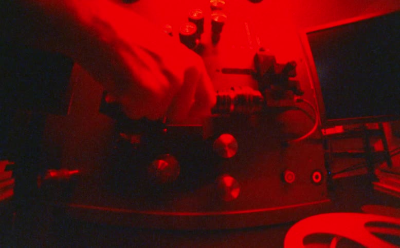 A close-up shot of a hand operating a vintage film editing machine bathed in shifting blue, red, and green lights