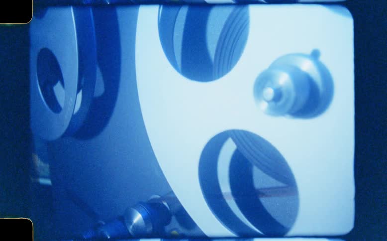 A retro super 8 film captures a close-up of a vintage movie projector's spinning reels with a classic blue hue