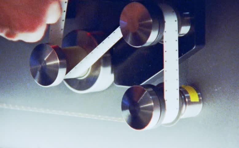 Close-up of a film technician's hands loading leader tape onto the metal rollers of a film processing machine
