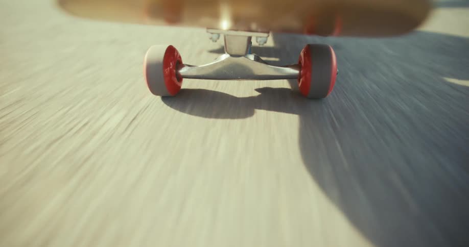 A low-angle, point-of-view shot captures the red wheels of a skateboard as it rolls quickly down a paved road