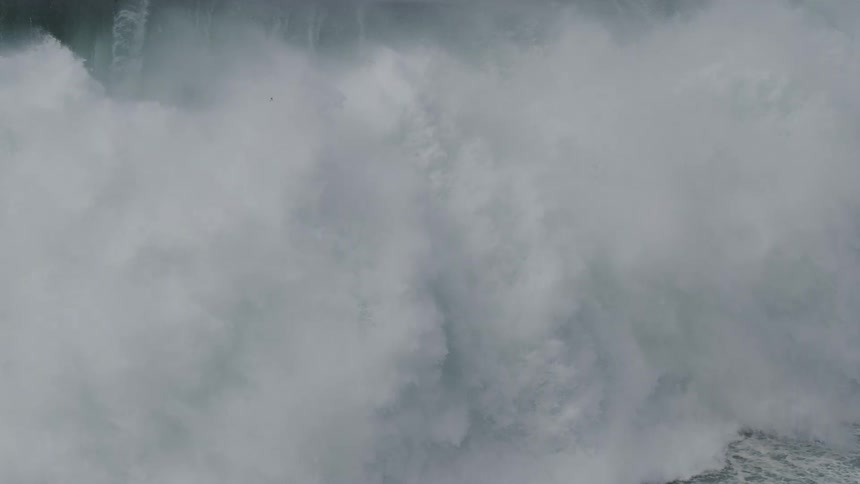 A massive, powerful ocean wave crashes in dramatic slow motion, turning into a turbulent wall of white water and spray