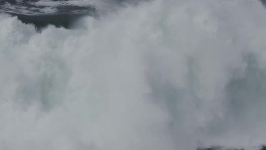 A powerful, dark ocean wave crashes in dramatic super slow motion, creating a massive explosion of white water