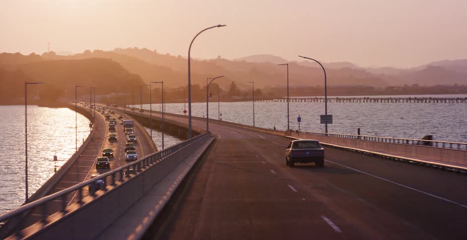 Driving across a scenic bridge over the water during a beautiful hazy golden hour sunset