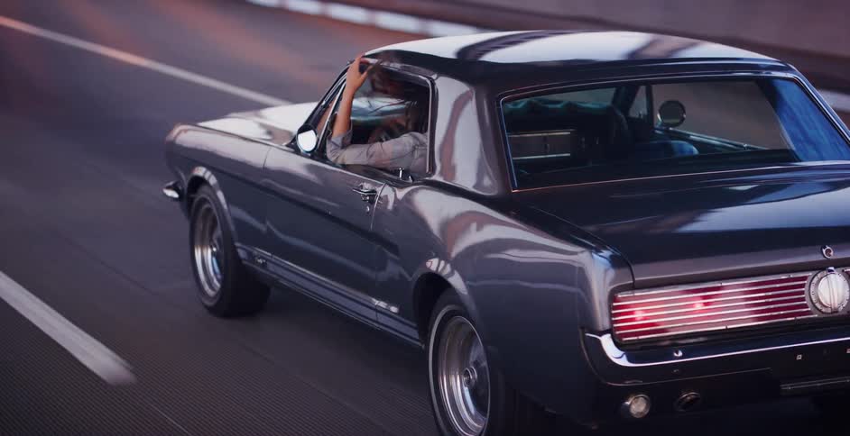 Slow motion shot captures a carefree driver with long, flowing hair cruising in a vintage muscle car down the highway