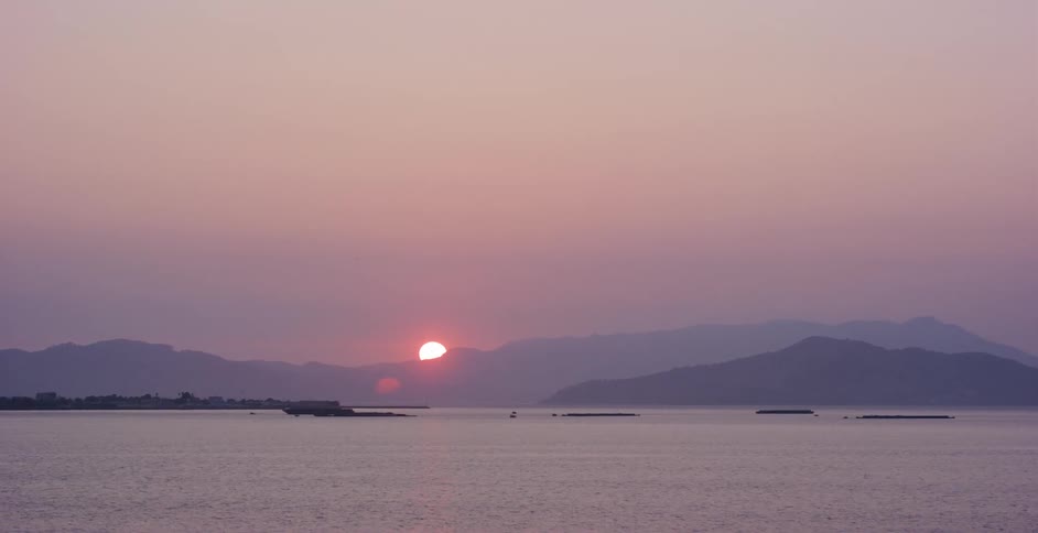 A beautiful purple and pink sunset descends behind distant mountains over a tranquil sea