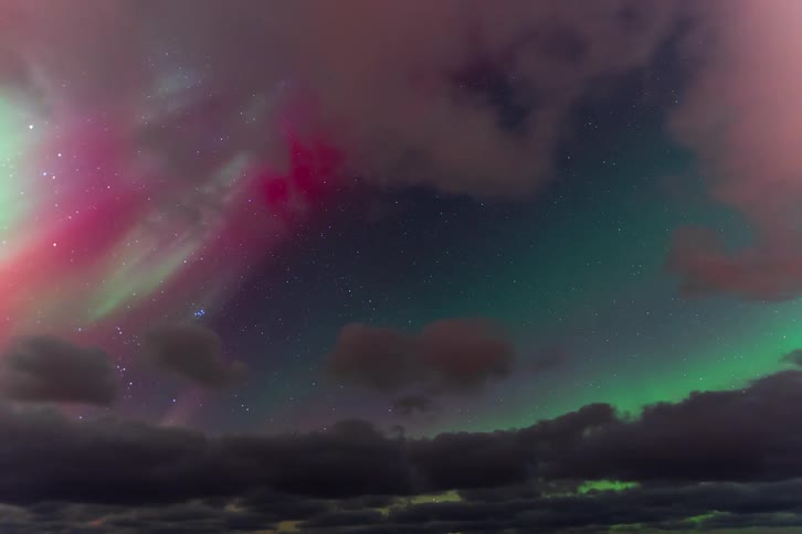 A stunning time-lapse of the vibrant green and purple Aurora Borealis dancing across a starry night sky as clouds drift by