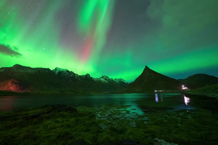 A stunning timelapse shows the vibrant green and purple Aurora Borealis dancing across the starry night sky above a mountain lake