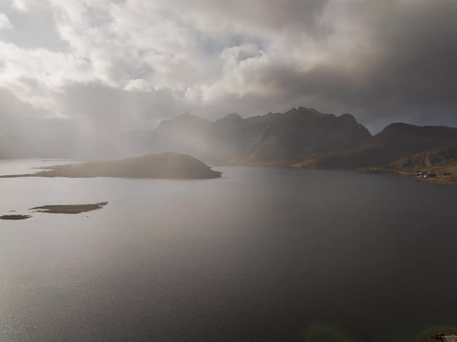 Sun rays break through dramatic storm clouds, illuminating a vast fjord surrounded by majestic mountains in an aerial view