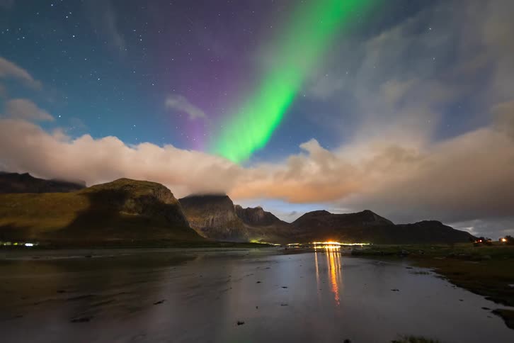 A breathtaking timelapse of the vibrant Northern Lights dancing above a mountainous landscape, with their colors reflecting in a still lake below